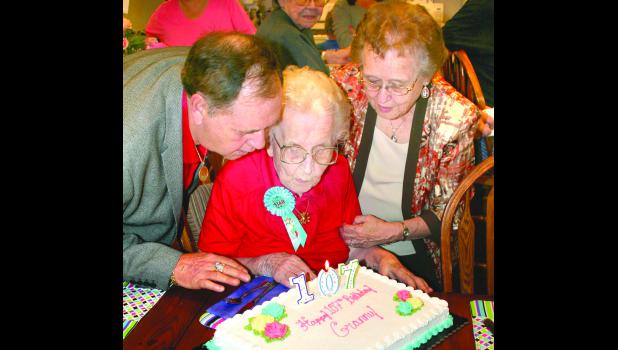 by Brian Sanders Mildred Vanek (center), a resident at the Glenn Moore Meadows assisted living facility south of Holton, celebrated her 107th birthday with a Friday afternoon party, in which grandson Craig Brunell (left) and daughter Bonnie Sporer (right) helped her blow out the candles on her birthday cake. Vanek's birthday was Sunday.