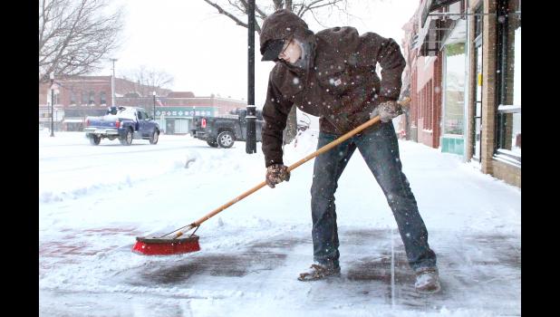 After a snowstorm late last Wednesday and early Thursday dumped about six inches of snow on the Holton area, some youngsters who got the day off from school were put to work removing snow from sidewalks and driveways. Luke Gallagher, a freshman at Holton High School, was no exception, sweeping snow from the sidewalk in front of Lifetime Eye Care on the south side of Holton’s Town Square. (Photo by Brian Sanders)
