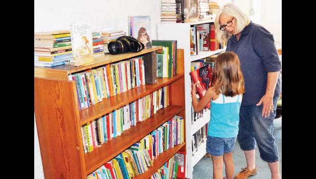 Vickie Wold (right), one of the organizers for the new free public library in Denison, helped Penny Hopkins, 7, select a book to check out during the library’s grand opening on Friday. (Photo by Ali Holcomb)