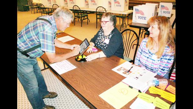 As Roy Hallauer (left) signed in to cast a vote in the 2016 primary election at the Jackson County Courthouse over the lunch hour on Tuesday, election volunteer Karen Welliever (center) instructed him on how to do so electronically while volunteer Mary Schulz looked on. (Photo by Brian Sanders)