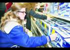 Holton High School junior Emma Wittmer (left) and senior Sonora Sheldon spent part of Tuesday morning placing stickers on packages of beer at Ron’s IGA and other businesses in Holton as part of the “Sticker Shock” campaign. Wittmer, Sheldon and other volunteers placed the stickers to warn adults about the consequences of buying alcoholic beverages for anyone under 21
